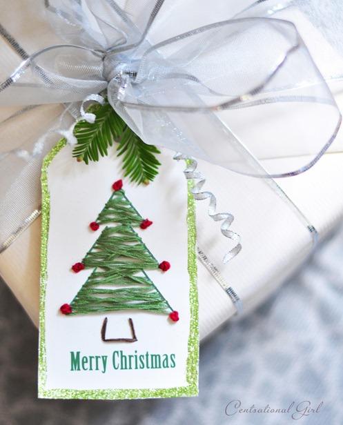 A white gift tag stitched with a green thread Christmas tree and red knots, tied to a cream wrapped parcel