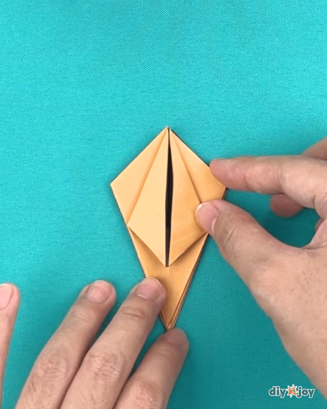 How can we make lily paper flowers, a folding step showing the middle side folds being pulled gently open
