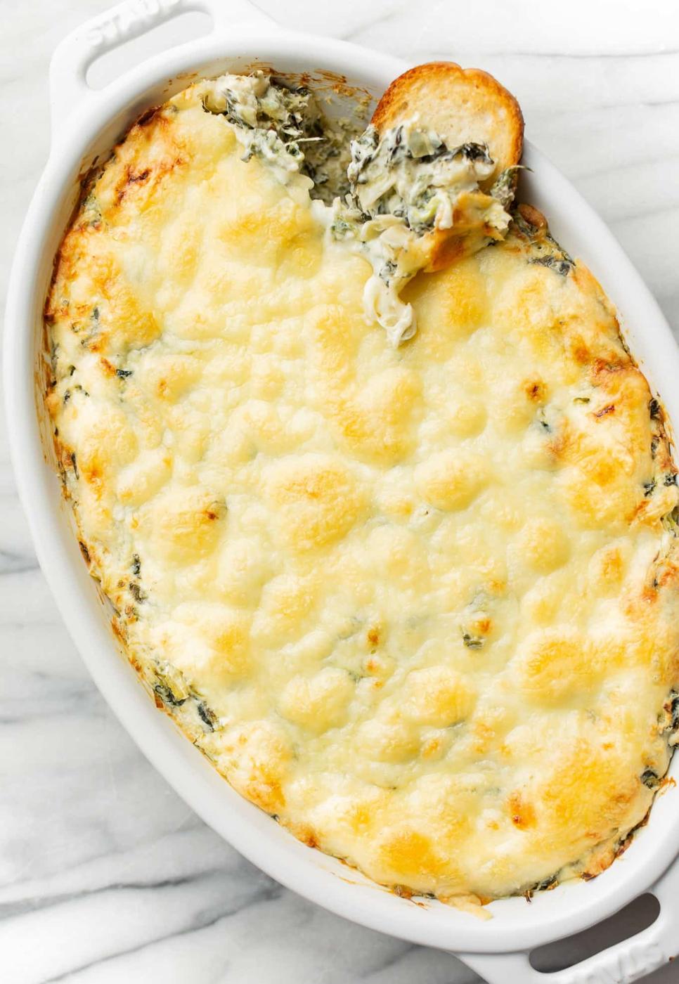 Hot spinach artichoke dip baked in an oval dish with browned melted mozzarella bubbling across the top