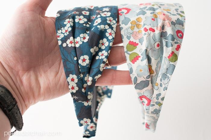 Hand holding two fabric covered headbands in small blue and pink floral prints against a plain white background