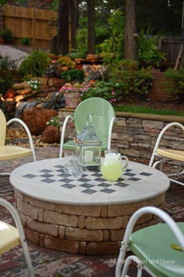 DIY firepit cover, a round gray checkerboard top on a stacked stone fire pit set with lemonade, glasses and a lantern