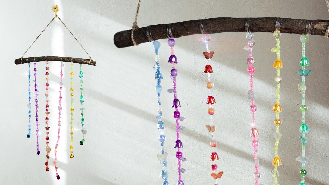 Beaded wind chime of colorful glass flower and butterfly bead strands hanging from a bare branch on a white wall