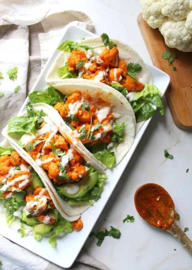 Three vegan buffalo cauliflower tacos on a white platter with romaine, avocado, ranch drizzle and cilantro