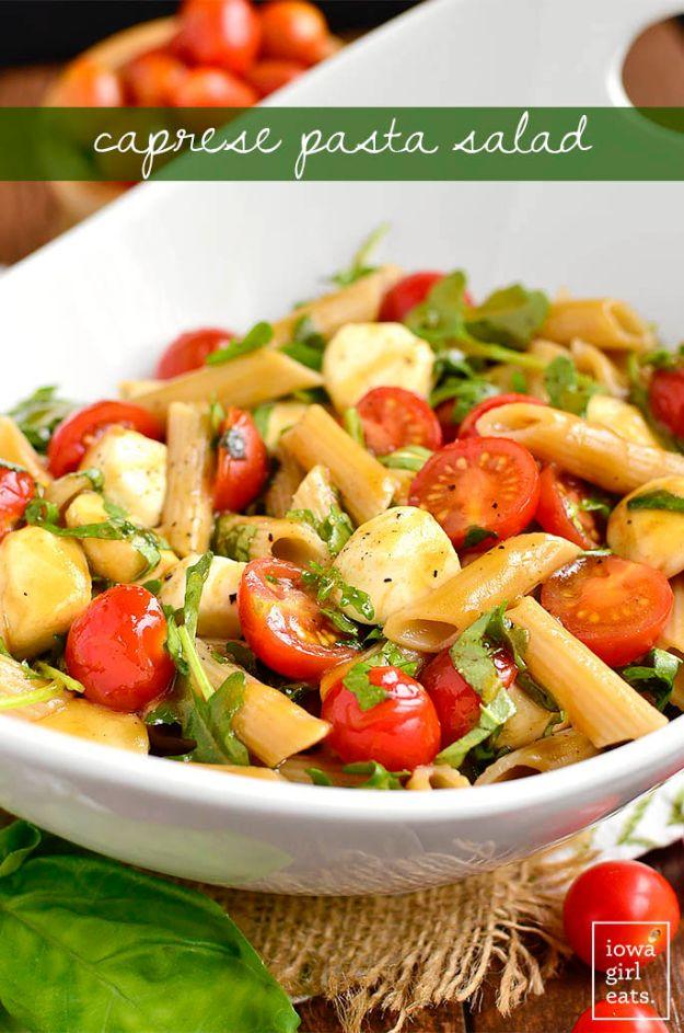 Caprese pasta salad in a white bowl with cherry tomatoes, mozzarella pearls, arugula and fresh basil