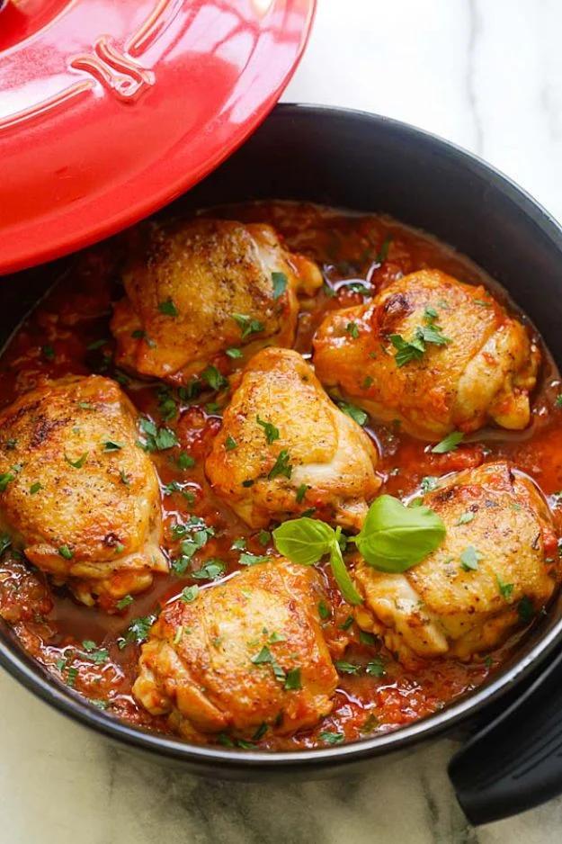 Italian braised chicken thighs simmering in a tomato and fresh basil sauce in a heavy covered braising pan