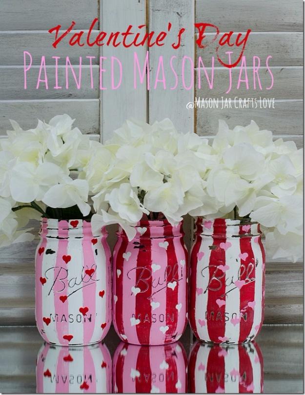 Painted and distressed mason jars with heart cutouts filled with flowers, a DIY Valentine decor idea