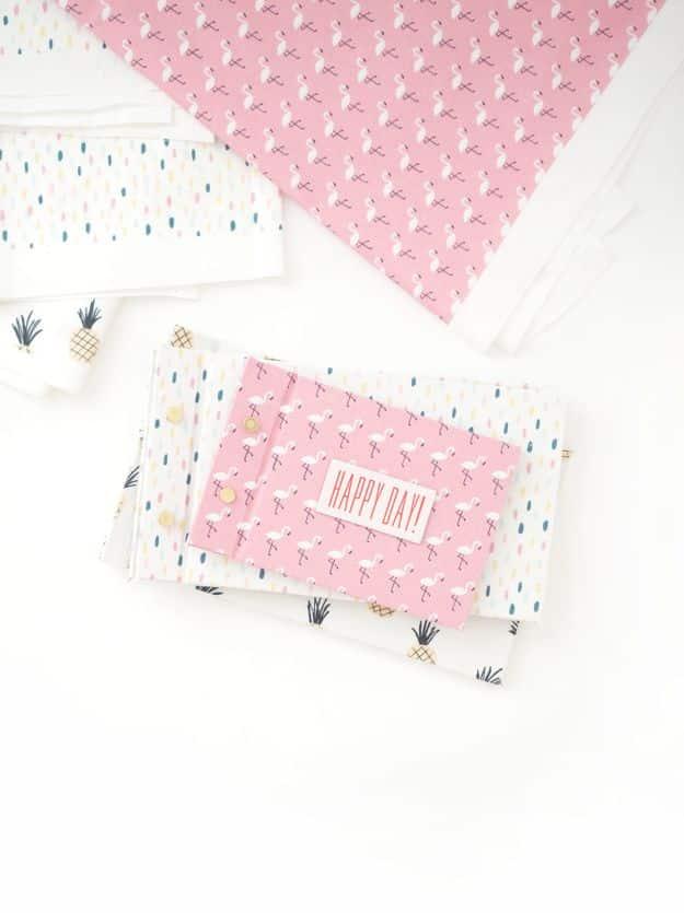 Easy DIY scrapbook journals covered in pink flamingo print fabric with a Happy Day label, on a stack of patterned fabrics