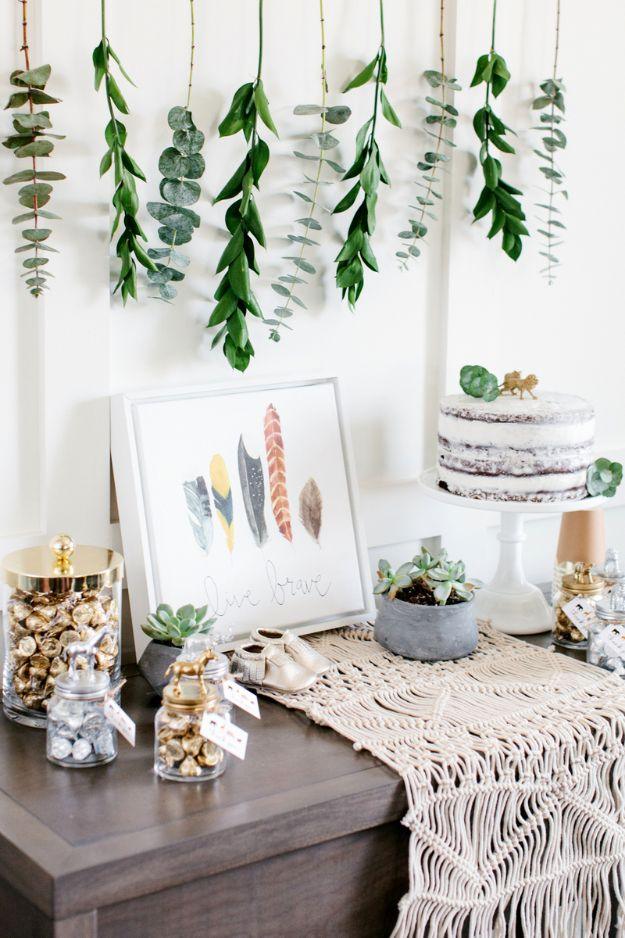 DIY baby shower decoration table with gold lidded animal favor jars, hanging eucalyptus and a naked cake on a stand