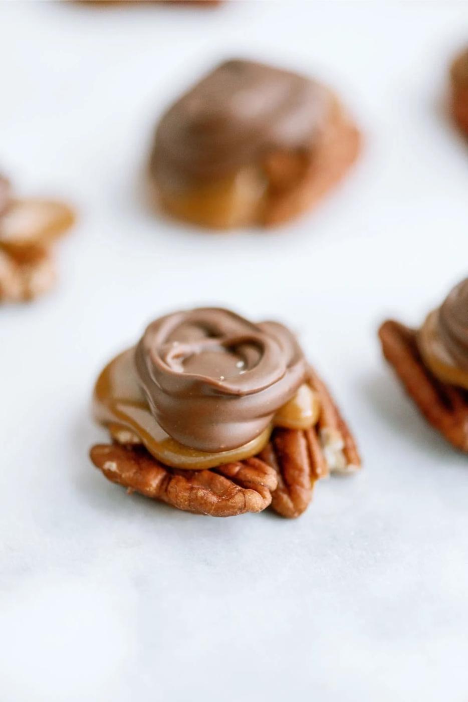 Close up of a homemade turtle candy with pecans, a layer of soft caramel and a swirl of milk chocolate on white marble