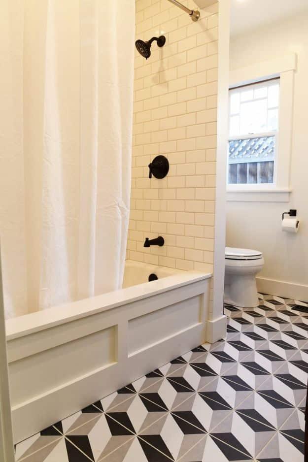 White bathtub with a panelled apron front and black fixtures, beside a geometric black and white tile floor