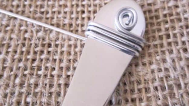 Close up of silver craft wire coiled and wrapped tightly around a plain flatware handle on a burlap background