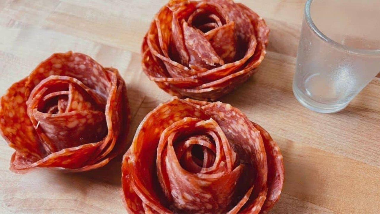 Salami roses made with a shot glass, folded pepperoni rounds arranged into flower shapes on a charcuterie board