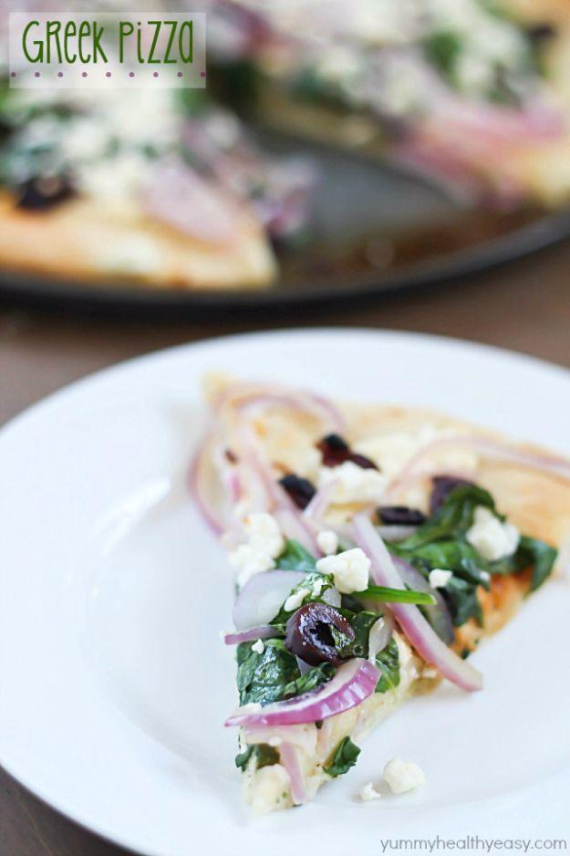 Slice of Greek pizza on a white plate with spinach, red onion rings, feta crumbles and kalamata olives