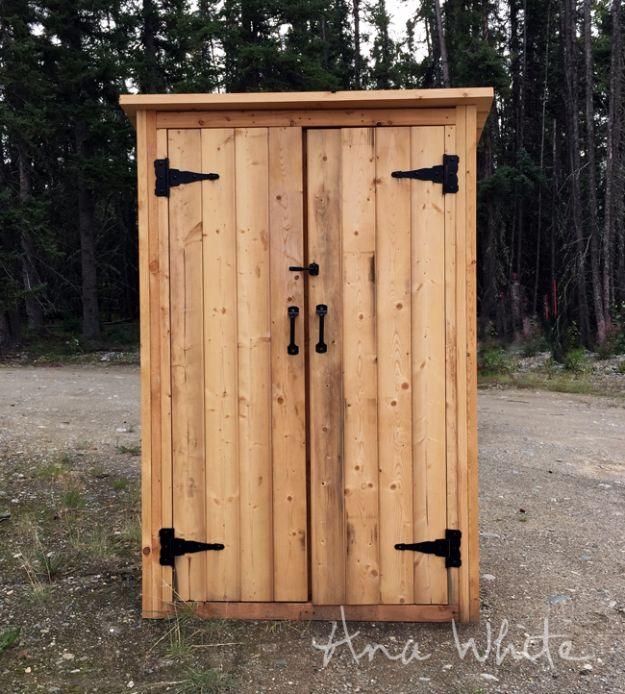 Small outdoor shed, a tall narrow cedar shed with double board doors and black gate hinges standing on gravel in woods