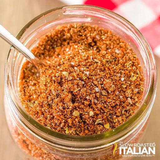 Wide mouth mason jar of reddish brown homemade barbecue rub with a spoon of the spice blend beside it