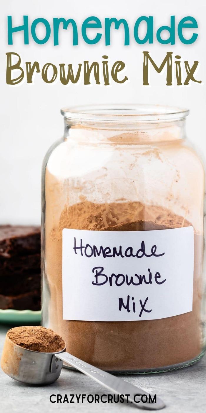 Tall glass jar of layered homemade brownie mix with cocoa and sugar stripes, baked brownies stacked nearby