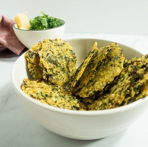 Four ingredient parmesan kale crisps stacked in a white bowl with a small dish of chopped kale behind