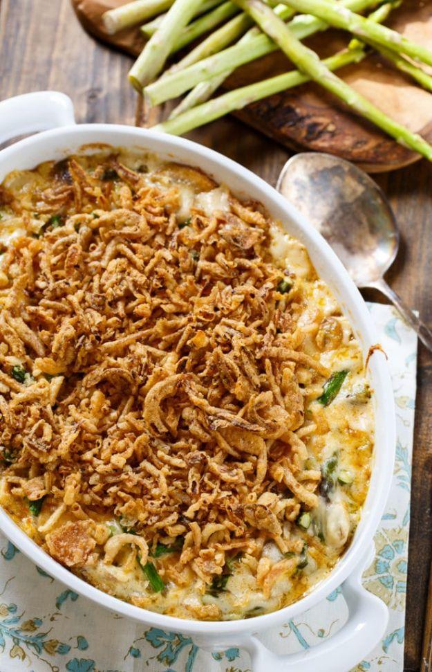 Asparagus casserole in a white oval baking dish topped with golden french fried onions, raw spears behind