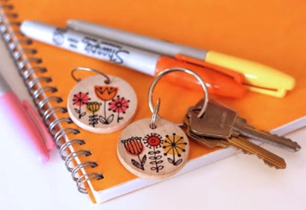 Wooden disks and sharpies, two small wooden disc keyrings drawn with folk flowers beside markers on an orange notebook