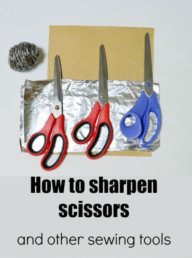 How to sharpen scissors, three pairs of scissors beside foil, sandpaper and a steel wool pad on a grey background