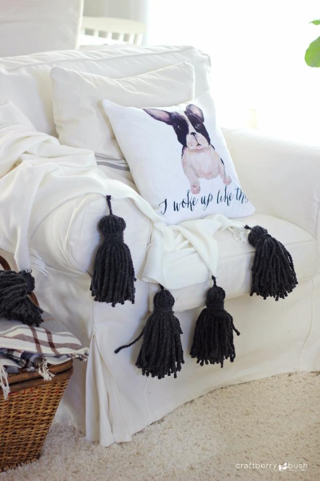 White slipcovered armchair with a throw edged in four thick charcoal yarn tassels beside a printed cushion