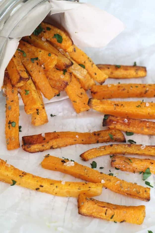Butternut squash fries spilling out of a paper cone onto parchment, seasoned with salt and chopped parsley