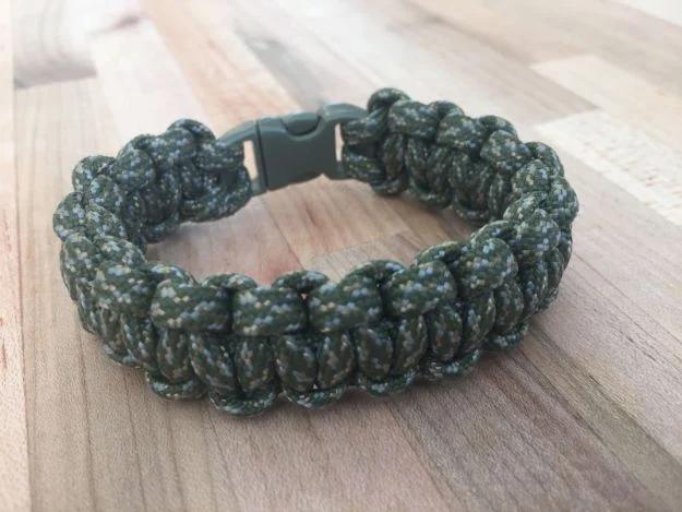 Olive and green camo paracord survival bracelet with a black side release buckle, on a pale wooden table