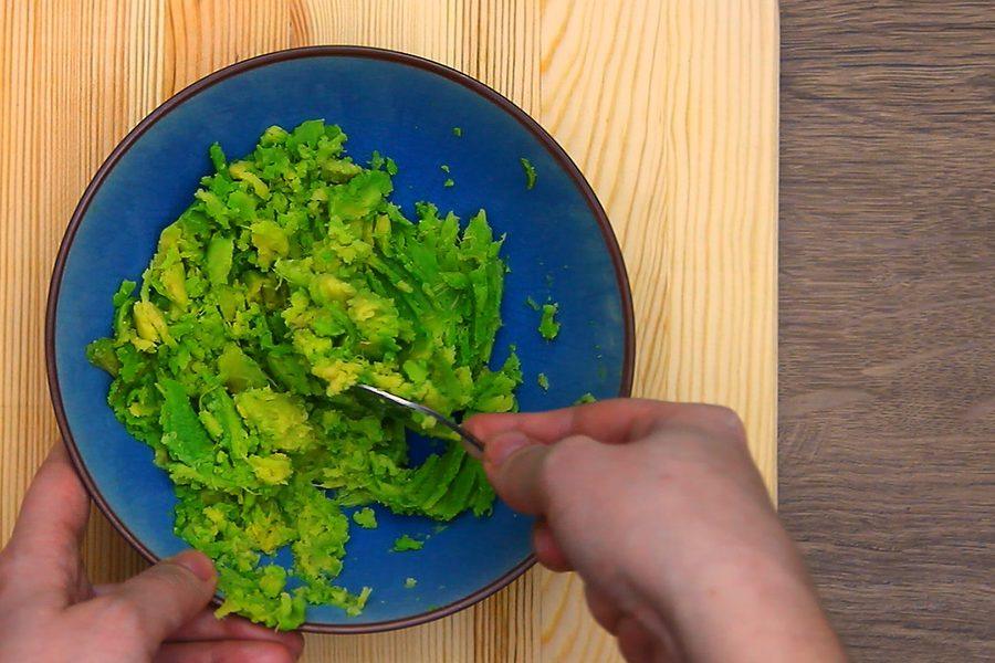 Mashing avocado with salt in a blue bowl