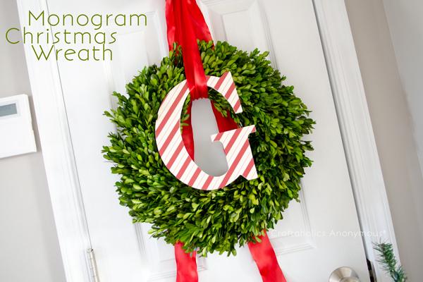 A boxwood wreath hanging on a white door from wide red ribbon with a candy cane striped monogram letter G in the center