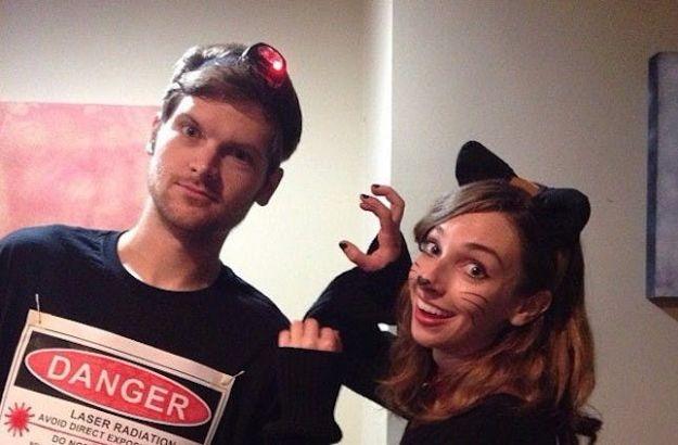 Cat and laser pointer couples costume with pinned black ears, a stuffed tail and a red headlamp with a warning sign