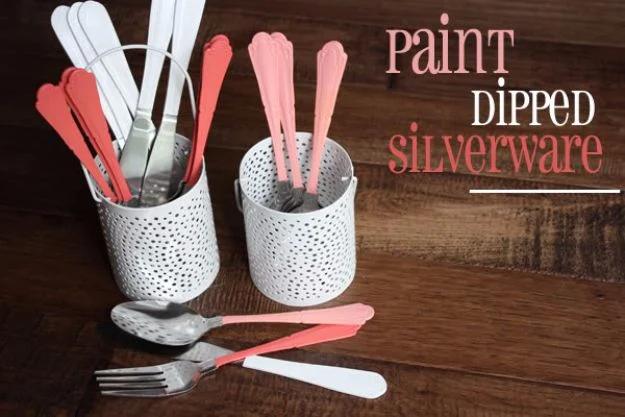 Coral, pink and white paint dipped forks, knives and spoons in two white metal caddies on a wood table