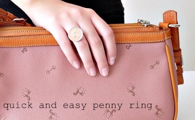 Penny ring on a hand resting on a pale pink leather handbag, one shiny coin set on a plain ring shank