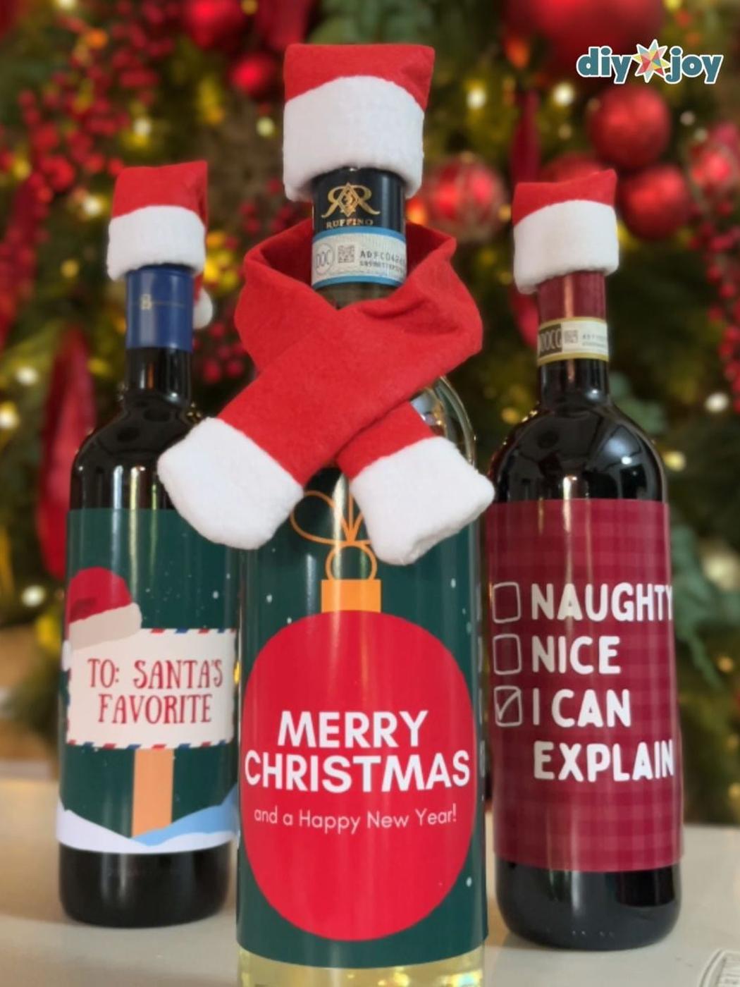 Three wine bottles in tiny felt Santa hats and a red scarf with printed labels reading Merry Christmas and I can explain