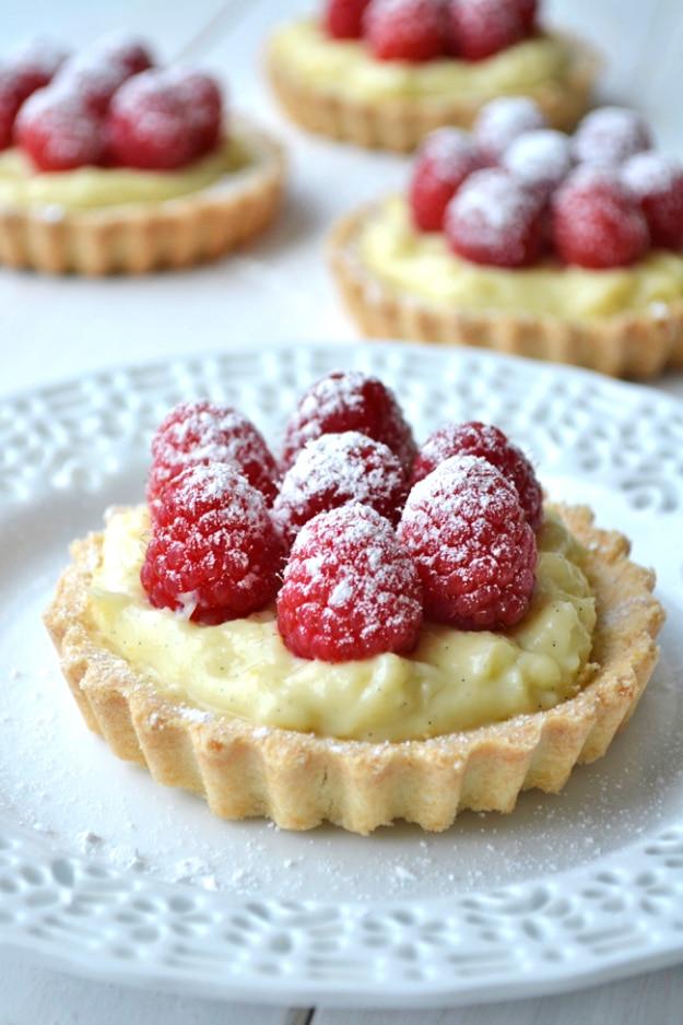 Raspberry vanilla bean cream tarts topped with fresh berries and powdered sugar, an elegant easy dessert idea