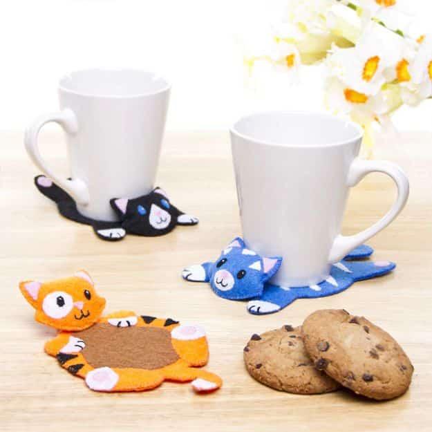 Super cute cat coasters, four felt cat coasters in black blue orange and white under white mugs beside two cookies