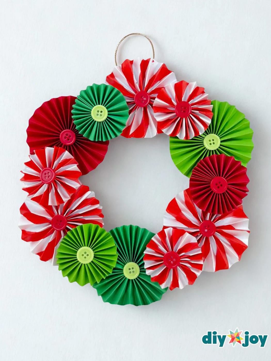 A wreath of accordion folded paper rosettes in red, green and candy cane stripes with button centers and a gold cord loop
