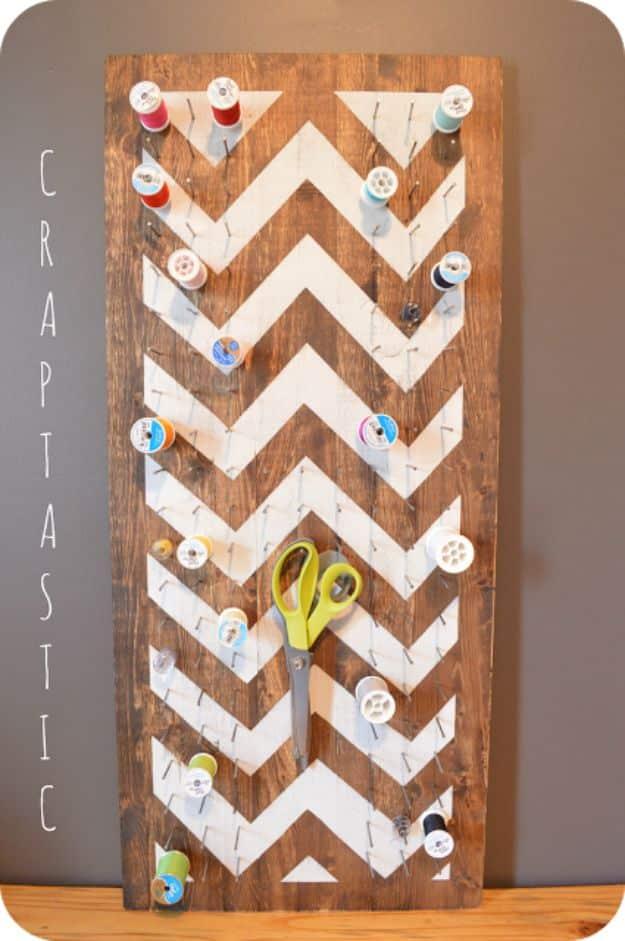 Dark stained board with a white chevron pattern, rows of thread spools on nails and a pair of green scissors hanging