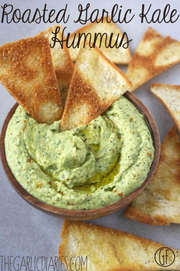 Roasted garlic kale hummus in a dark bowl with pita chips around it under a handwritten title graphic