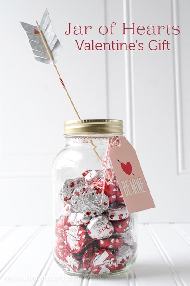 Mason jar packed with small folded paper hearts each carrying a handwritten reason for Valentine's in pink and red