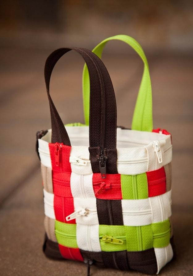 Small upright tote bag woven from red, lime, cream and brown zippers with two zipper handles on a stone floor