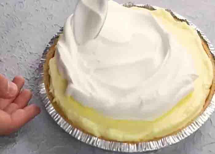 Adding the whipped cream on top of the lemon pudding pie