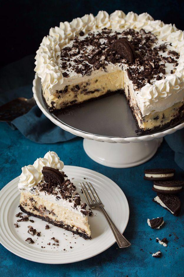 Cookies and cream cheesecake on a white pedestal stand with crushed Oreos, one wedge out on a plate, teal surface