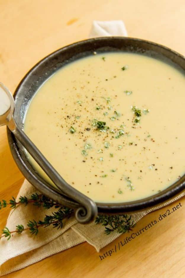 Caramelized onion roasted garlic bisque in a dark rustic bowl, pale and smooth with chopped herbs on top