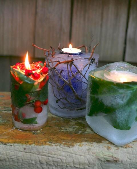 Three ice lanterns with red berries, leaves and twigs frozen inside, glowing with tea lights on a weathered wooden bench