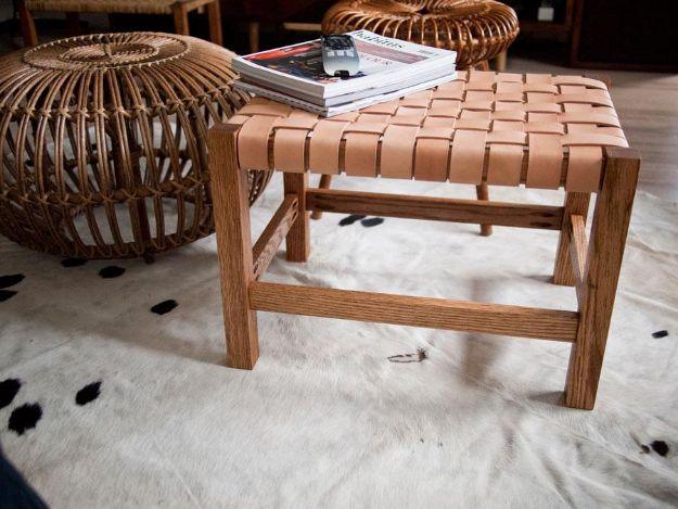 Small wooden bench with a woven natural leather strap seat on a white cowhide rug beside a round rattan pouf and magazines