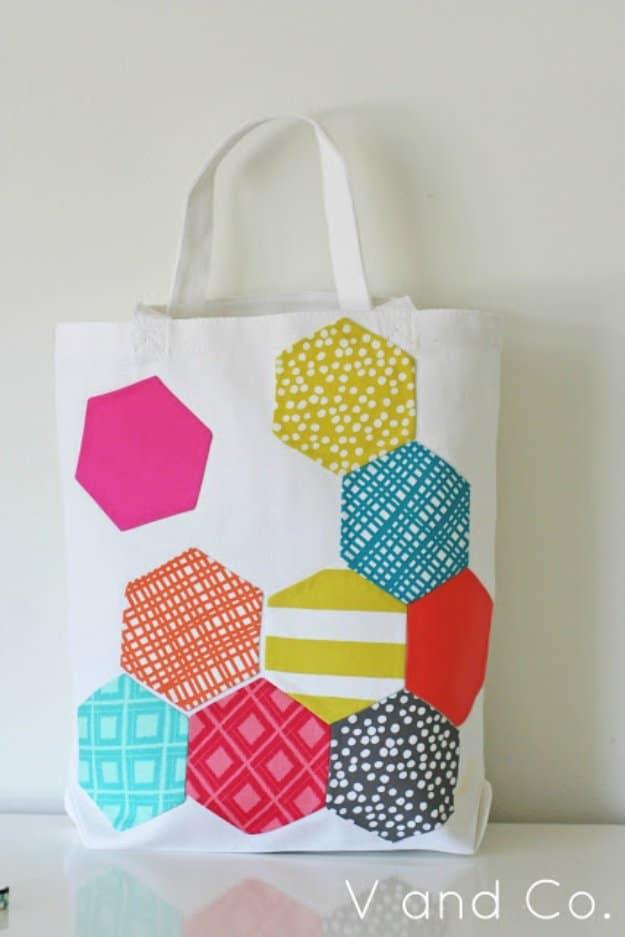 Canvas tote bag appliqued with nine fabric scrap hexagons in pink, teal and mustard prints, a bright DIY scrap sewing project