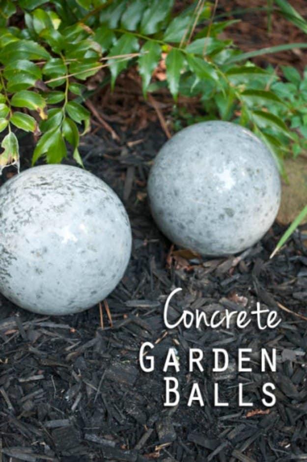 DIY concrete garden balls, two mottled pale cement spheres sitting in dark mulch beside green garden foliage