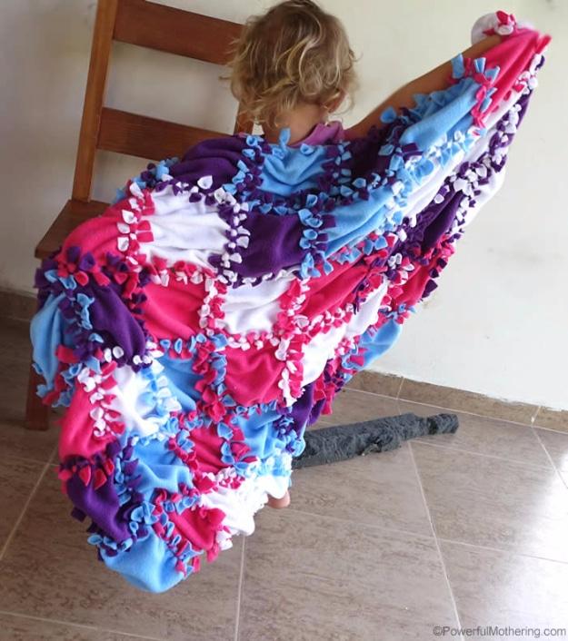Young child seen from behind holding up a knotted fleece patchwork blanket in pink, purple, blue and white