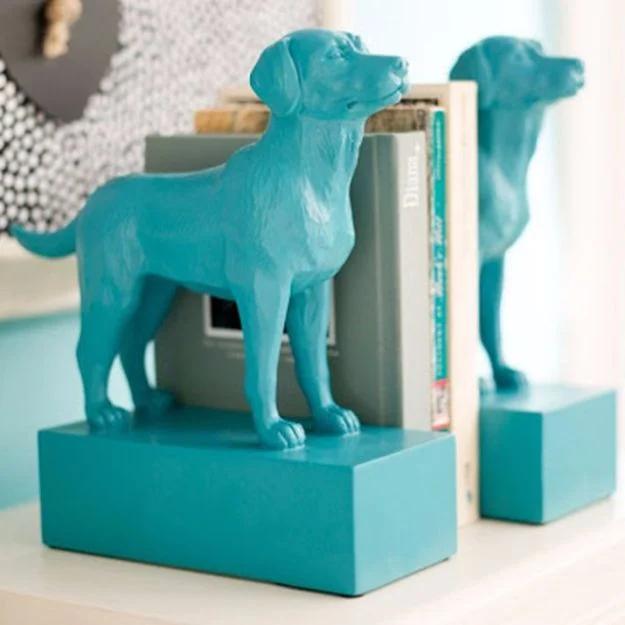 Pair of bookends made from toy dogs on rectangular blocks, all spray painted glossy teal, holding books on a white shelf