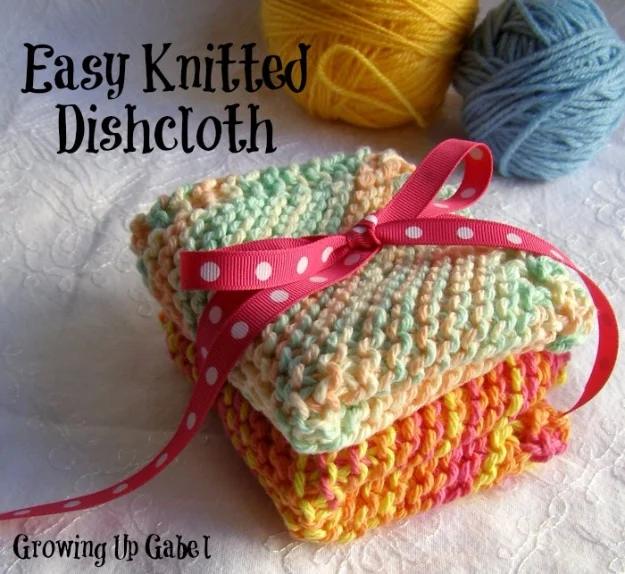 Stack of three knitted cotton dishcloths in pastel and orange tied with a pink polka dot ribbon beside yarn balls